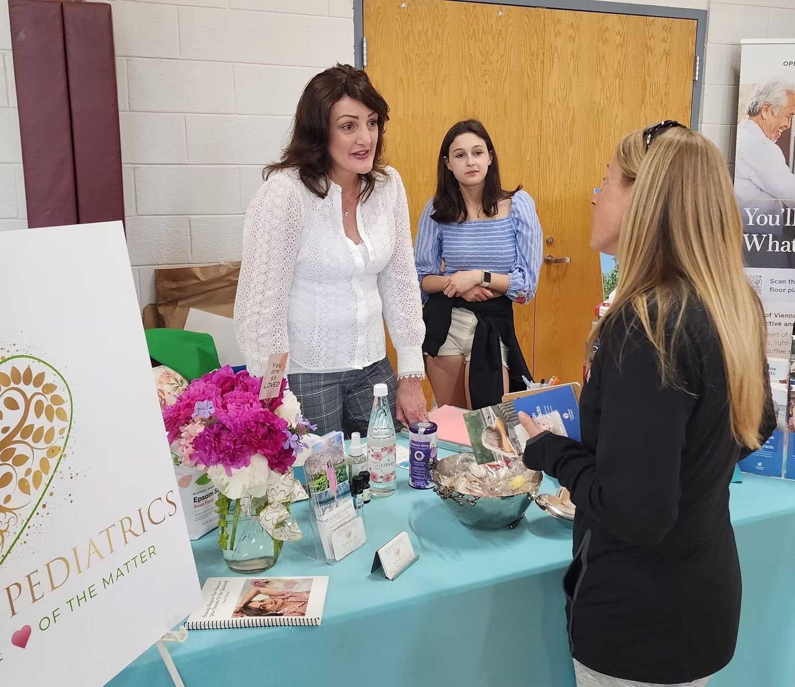 Exhibitors chatting with a visitor at a table with fresh flowers